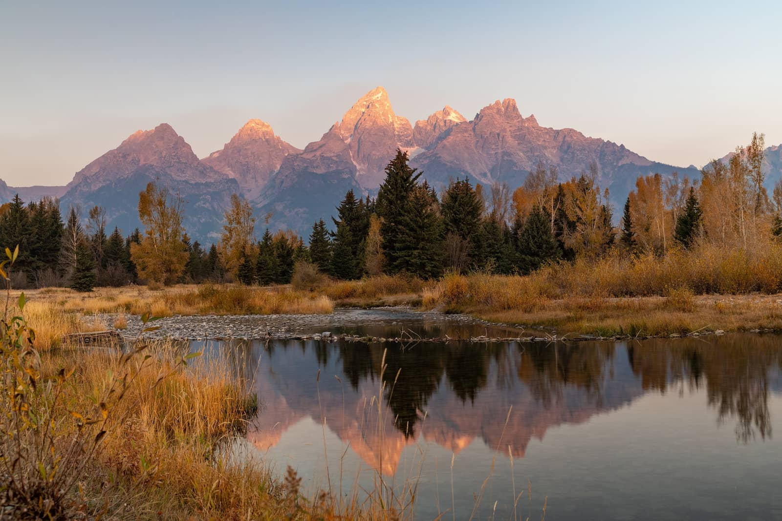 The Teton Range at sunrise, golden light reflecting across the Snake River in Wyoming